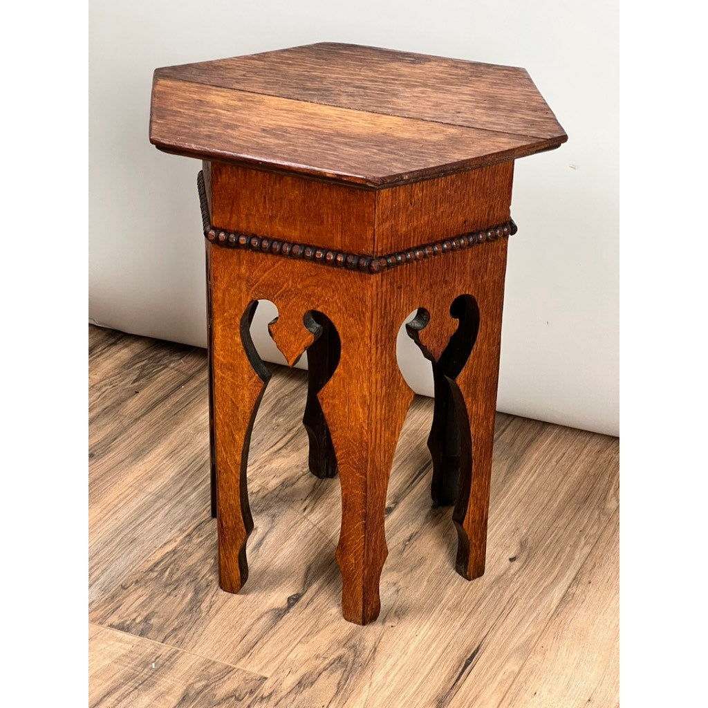 The Antique Arts & Crafts Small Oak Occasional Table c. 1910 features intricate cut-out leg designs, decorative edge beading, and a rich brown finish. This antique sits on a wood-patterned floor against a light wall. Brand: None/Unknown.