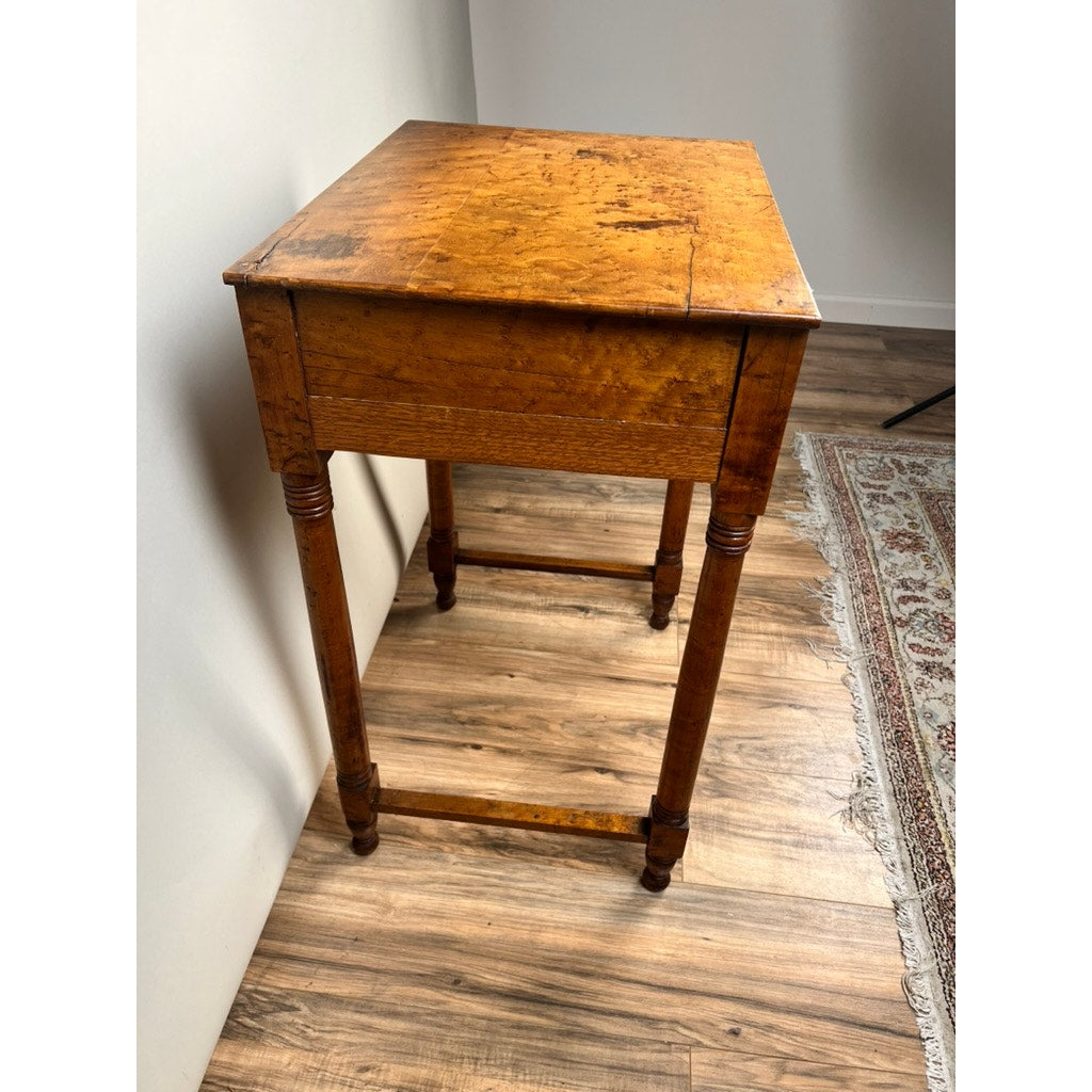An Antique Sheraton Birdseye Maple One Drawer Stand from the early 19th century features a rectangular top, turned legs, and a stretcher, shown on a wood floor by a rug in a brightly lit room. Brand unknown.