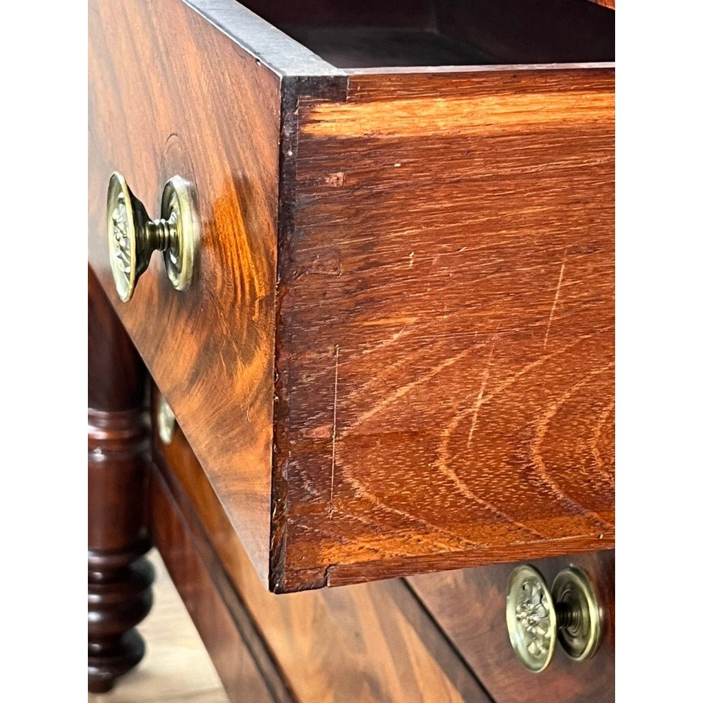 Close-up of an open drawer on the Antique American Empire Albany Four Drawer Chest c. 1840, highlighting flame mahogany grain, brass handles, and dovetail joinery; another drawer and carved leg are partially visible below.