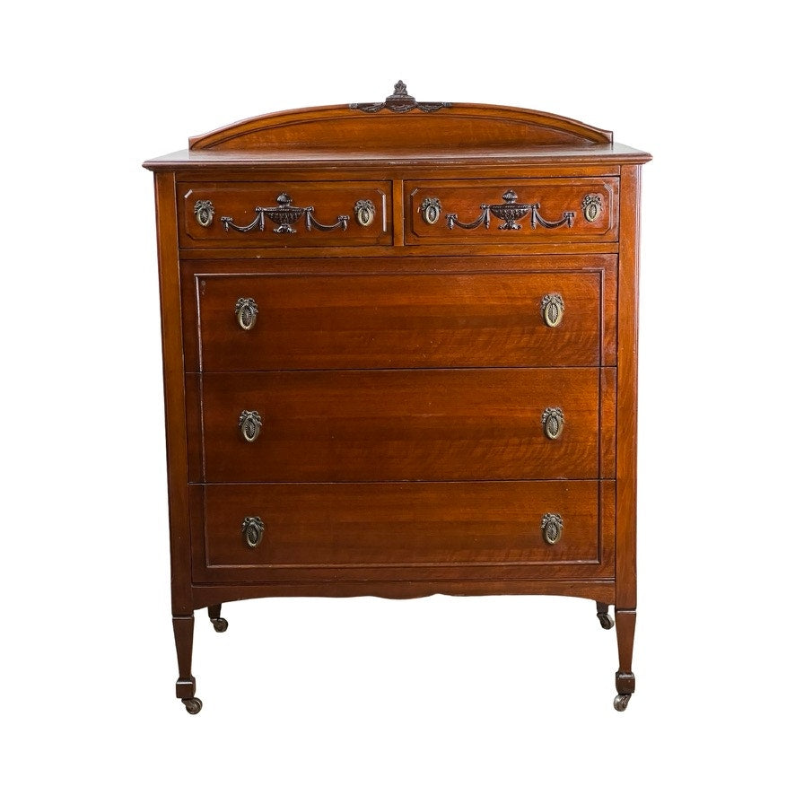 This Antique Depression Era Mahogany Two Over Three Chest of Drawers (c. 1930s) features four drawers with ornate metal handles, decorative carvings, slender legs with small wheels, and a decorative backboard. Brand unknown.