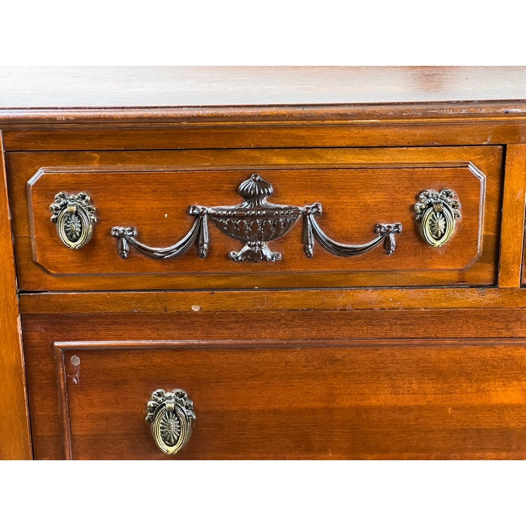 Close-up of an Antique Depression Era Mahogany Two Over Three Chest of Drawers c. 1930s, featuring ornate metal handles, decorative carvings with a central urn and garlands, oval side pulls, and a polished warm brown finish. Brand: None/Unknown.