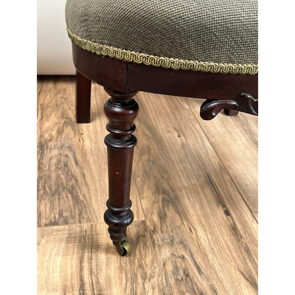 A close-up of an Antique Victorian Rococo Revival Carved Walnut Slipper Chair (late 19th c.), showing its intricately carved leg, original caster, and floral needlepoint seat—an elegant nod to timeless Victorian design. Brand: Unknown.