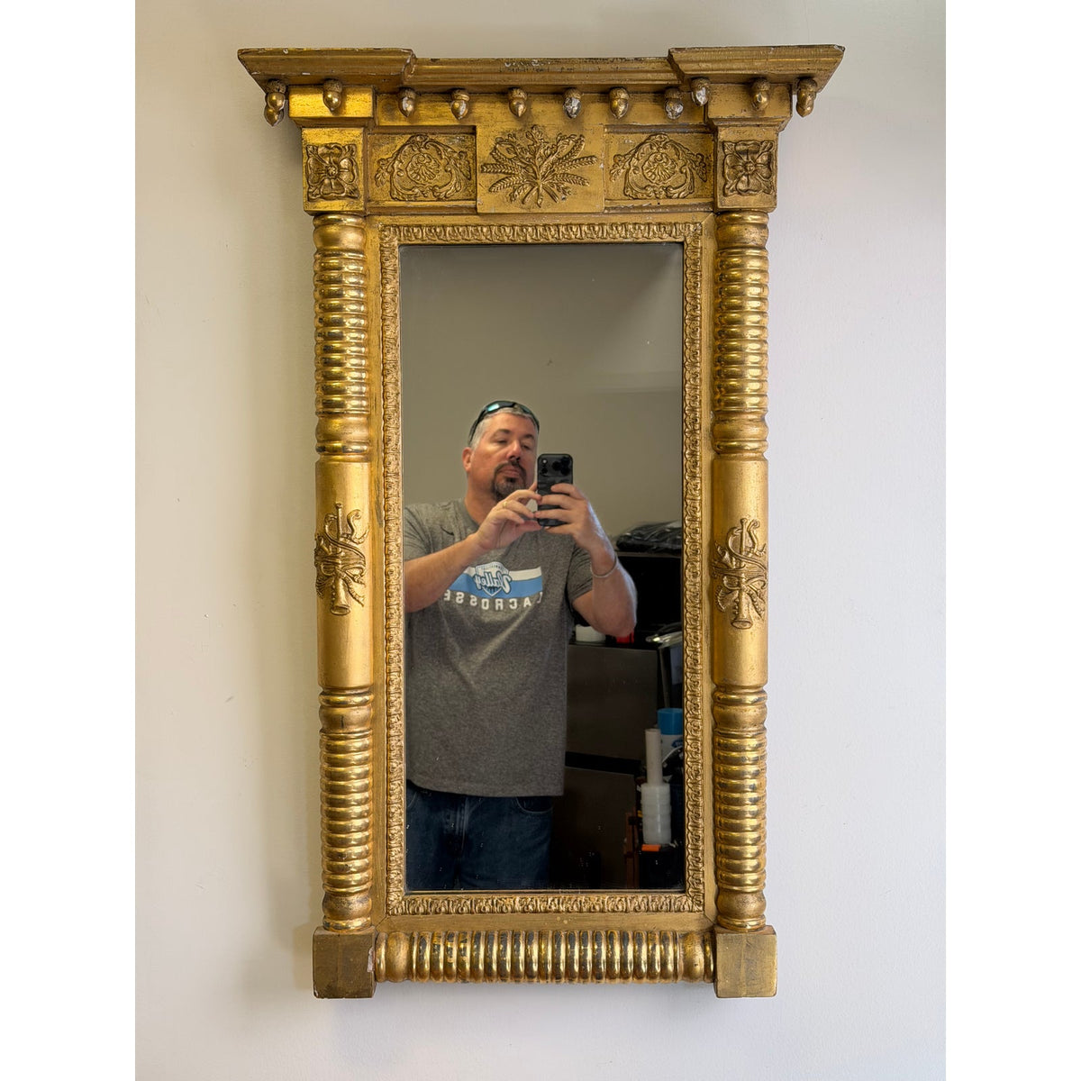 An American Federal Giltwood Pier Mirror, Possibly Massachusetts or New York, circa 1815–1830, is an ornate, rectangular 19th-century giltwood pier mirror featuring a heavy top cornice and columns along the sides.