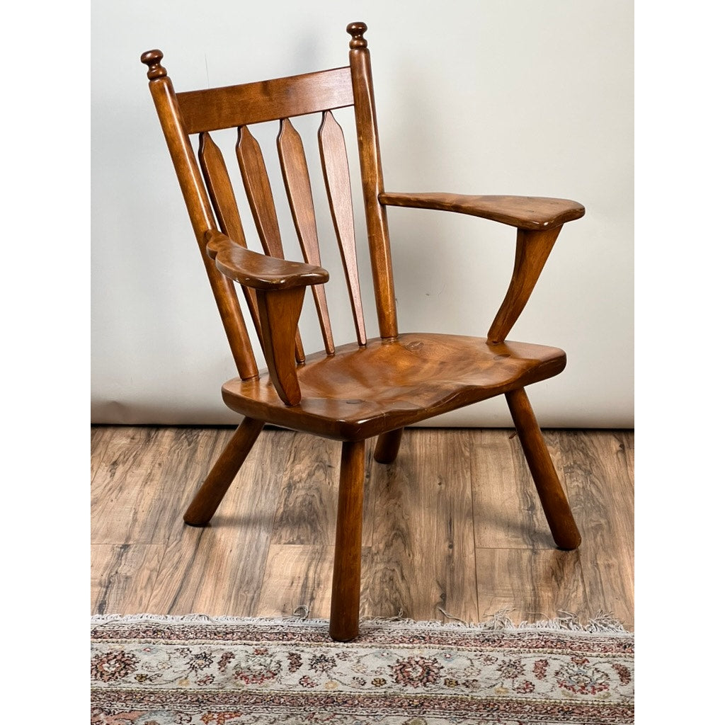 A Vintage Herman DeVries for Cushman No. 5-82 Rock Maple Easy Chair with a high back, vertical slats, wide sculpted armrests, and angled legs sits on a hardwood floor partially covered by a decorative rug.