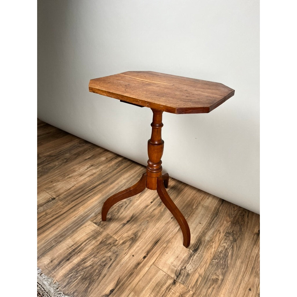 An Antique 19th Century Cut Corner Hepplewhite Candle Stand with an octagonal top, turned pedestal, and three curved legs stands on a wood-patterned floor against a plain white wall. Brand: None and/or Unknown.