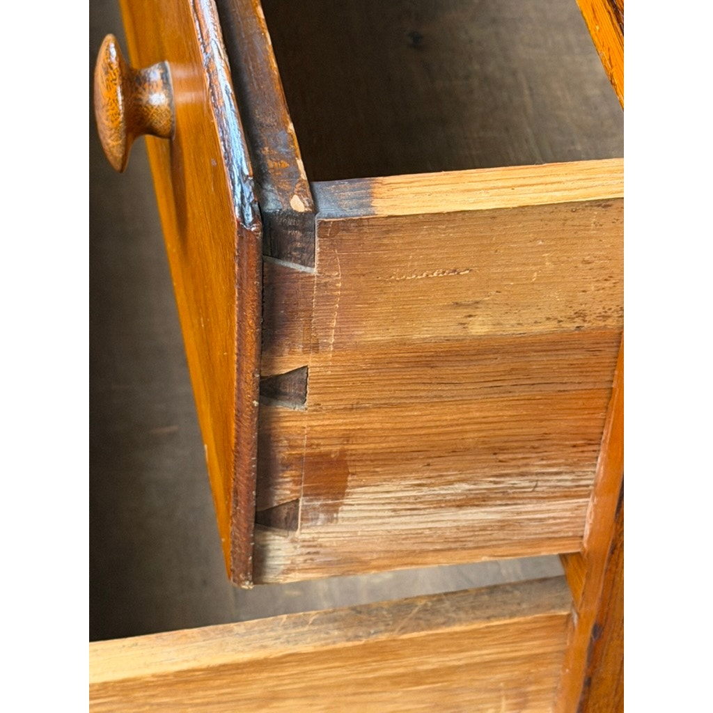 A close-up of a wooden drawer partially opened, revealing dovetail joints connecting the front to the side panel—a classic craftsmanship detail featured in this Late 18th Century New England Pine Two-Drawer Blanket Chest (c. 1780–1810) from Pearl City Antiques.