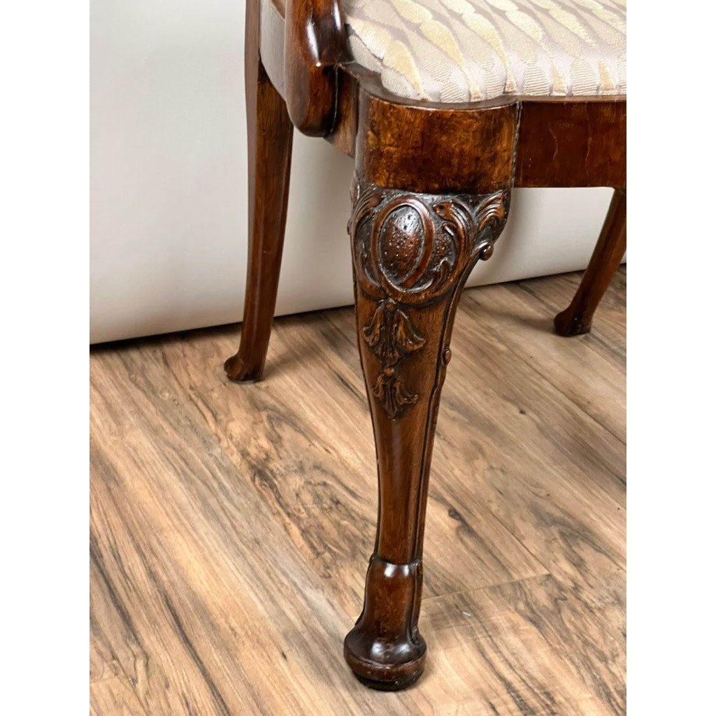Close-up of an Antique George III Mahogany Open Arm Chair (late 18th century), showing a carved leg with Chippendale floral and oval motifs and a patterned upholstered seat, displayed on a wood floor. Brand: Unknown.