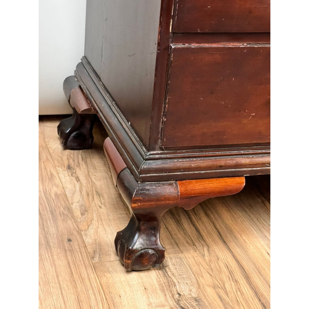 Close-up of the corner of an 18th Century New England Chippendale Cherry Slant Front Desk, Circa 1770–1790, featuring ornate claw foot legs resting on a hardwood floor. The cherry wood finish displays scuffs and scratches, emphasizing the desk’s vintage character and antique charm. Brand: Unknown.