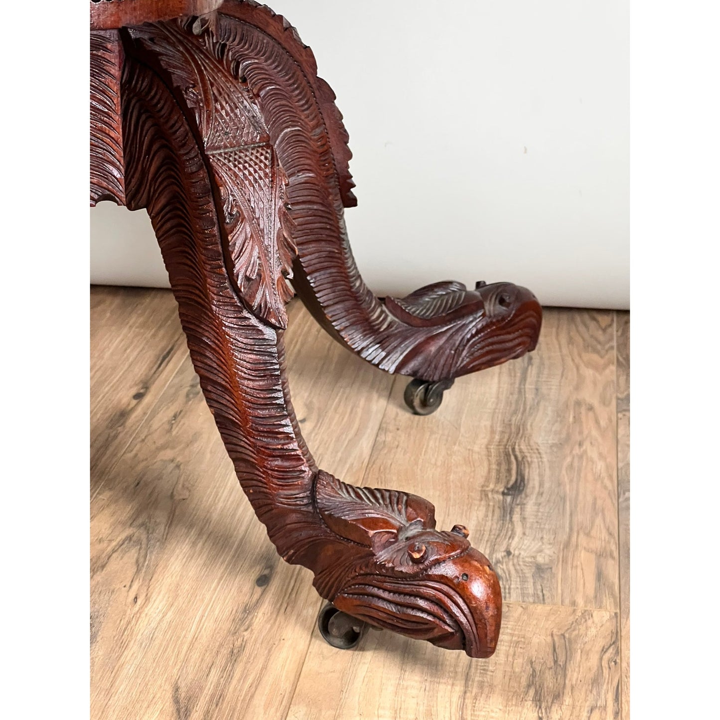 Close-up of the Antique American Empire Drop Leaf Table c. 1840, showcasing intricately carved eagle head and feather designs, with great eagle feet on wheels, set on a light wood floor against a plain white background.