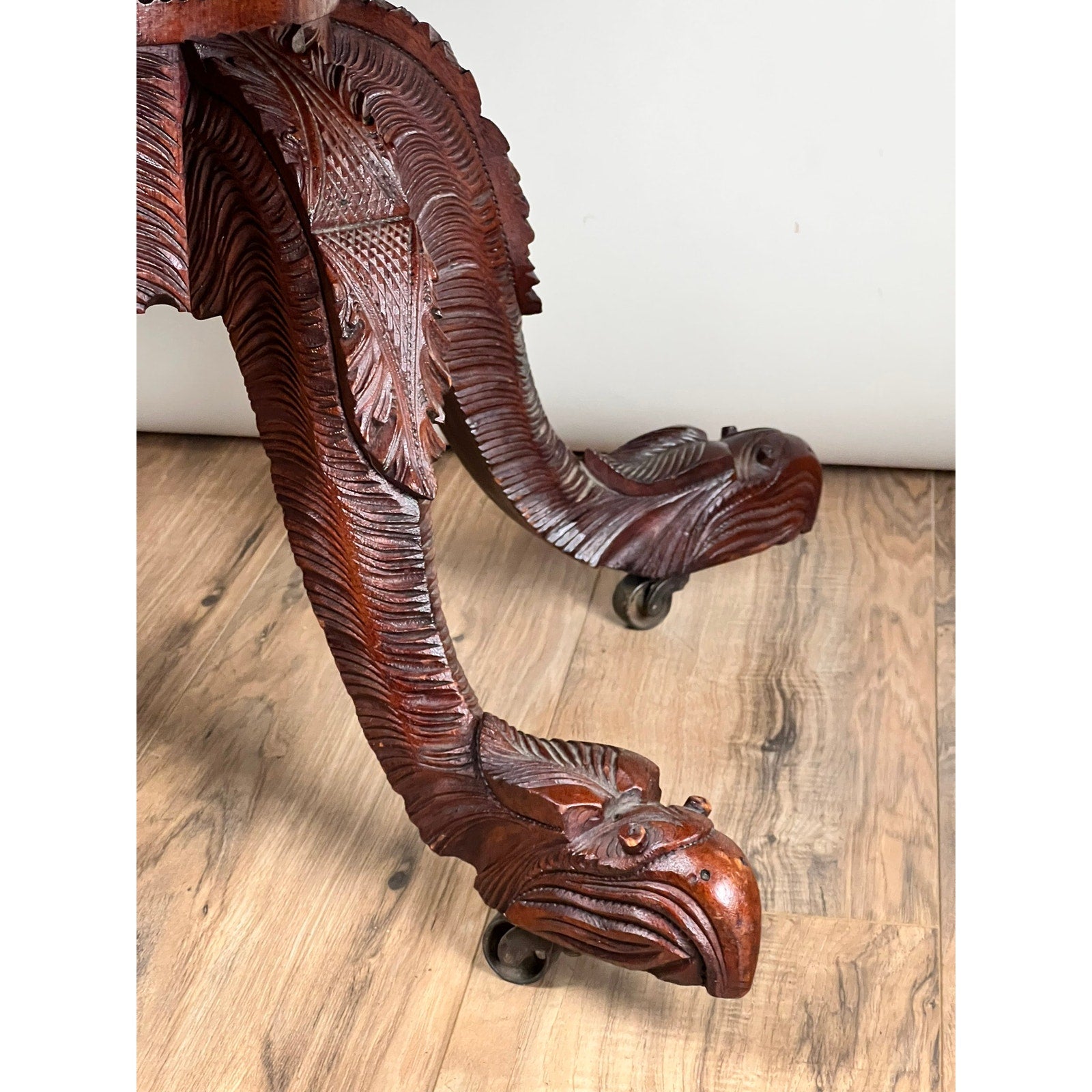 Close-up of the Antique American Empire Drop Leaf Table c. 1840, showcasing intricately carved eagle head and feather designs, with great eagle feet on wheels, set on a light wood floor against a plain white background.