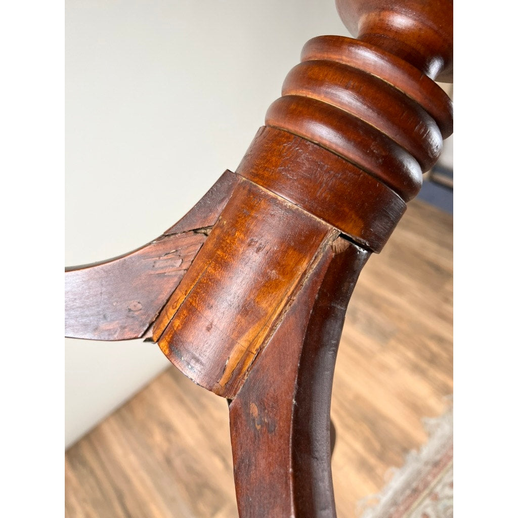 Close-up of a leg from an Antique Federal Period Cherry Hepplewhite Candle Stand (mid-19th century), showing a crack and worn varnish at the joint; wooden floor and patterned rug visible beneath. Brand unknown.