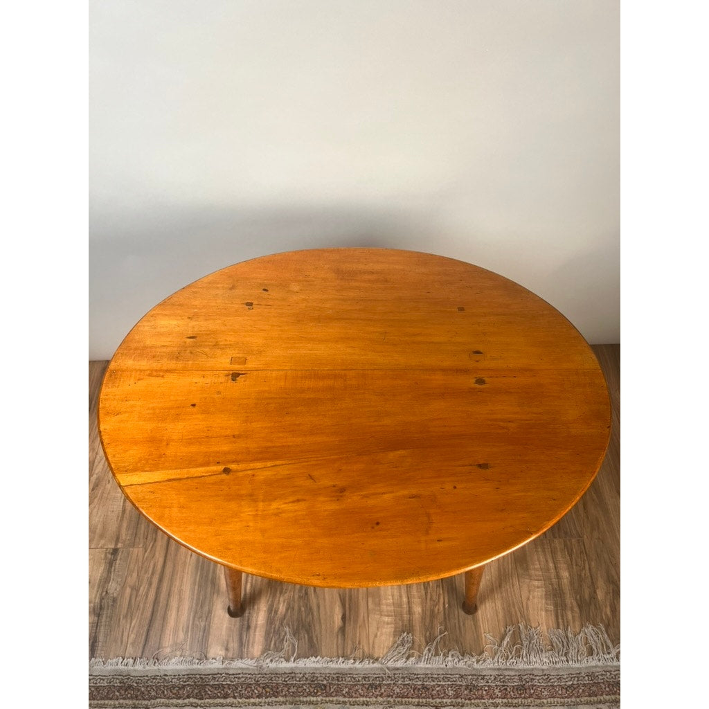 An Antique American Queen Anne Maple Tavern Table, New England, circa 1760–1790, with a polished round top and minor imperfections, stands on a wooden floor by a white wall, partly over a fringed patterned rug.