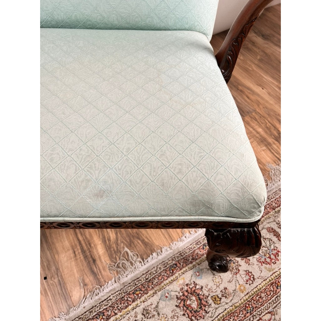 A close-up of an Antique George II Mahogany Gainsborough Open Arm Chair (c. Mid 19th Century) with light green upholstery, cabriole legs, and carved frame sits on a hardwood floor near a patterned rug; a faint stain marks the seat cushion.