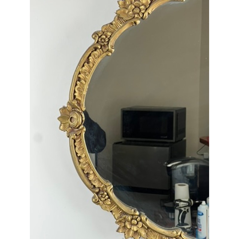 A partial view of an Antique Gilt Wood Oval Mirror (c. Early 20th Century) reflects a microwave, mini fridge, and various kitchen items on a counter against a plain wall.