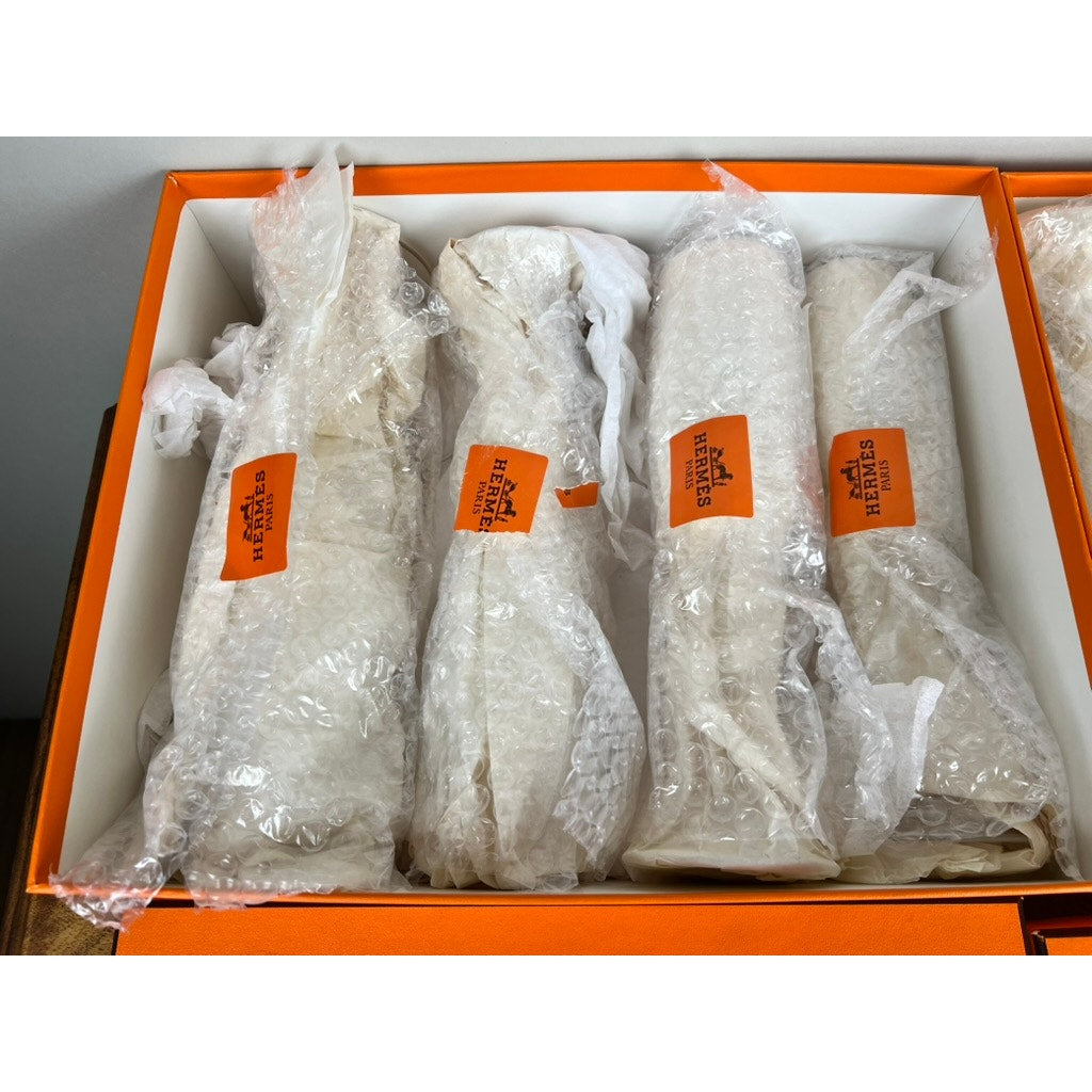Eight Hermès crystal champagne flutes by Saint Louis France (10.5") are side by side, each wrapped in bubble wrap with an orange Hermès label, displayed in a white and orange box—luxurious collectible glassware from Hermès.