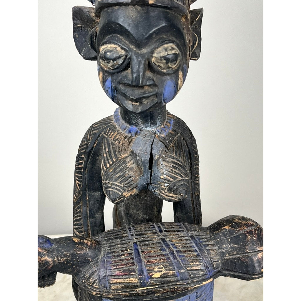 A close-up of an Antique Igbo Ikenga Shrine Figure, probably from Nigeria, highlights its detailed carved features, intricate patterns, blue paint accents, and a textured object held by the aged West African statue. Brand: Unknown.