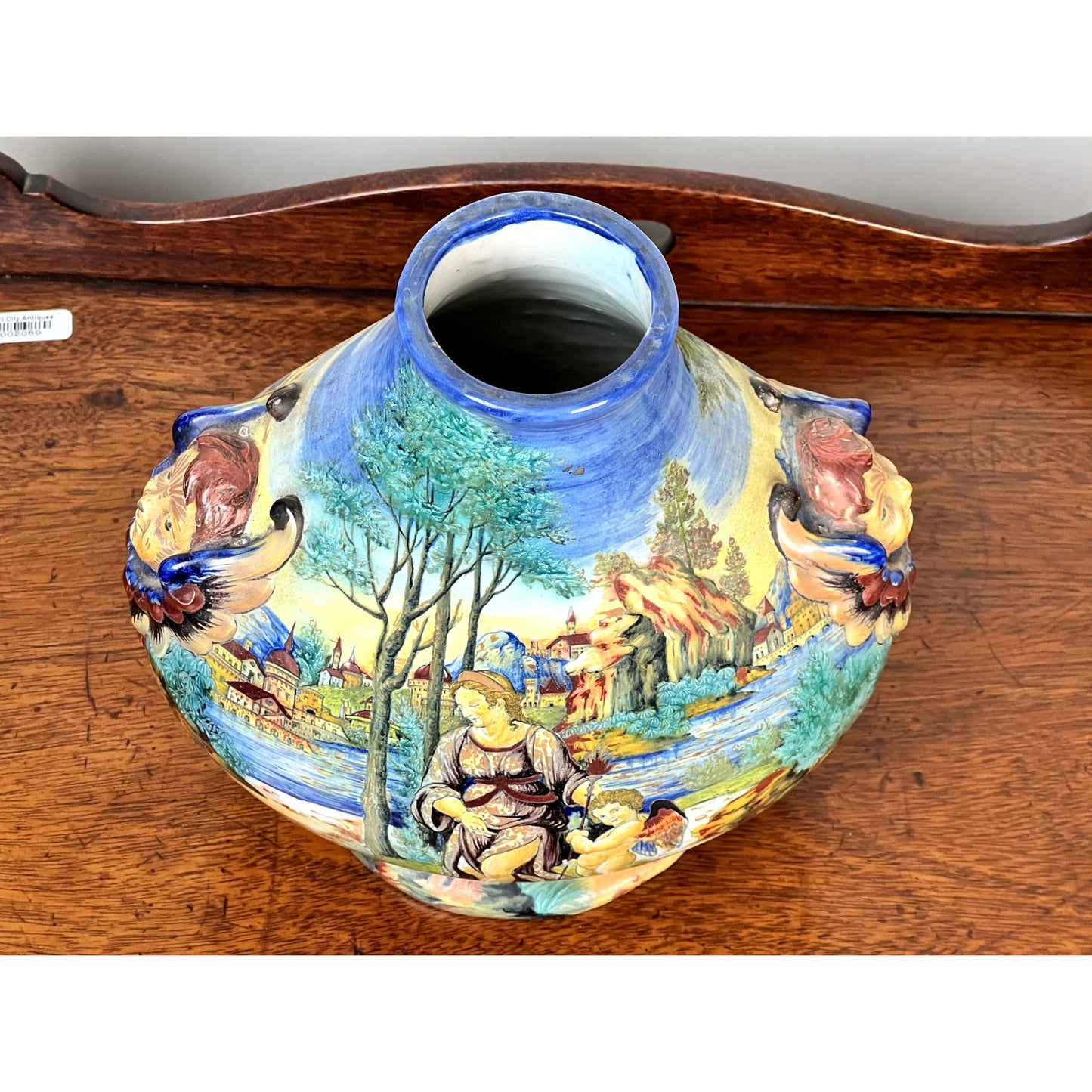 Antique Italian Renaissance Revival hand-painted maiolica vase (c. 1920-1940) with colorful scenes, wide mouth, and winged putti handles, resting on a wooden surface. Brand unknown.