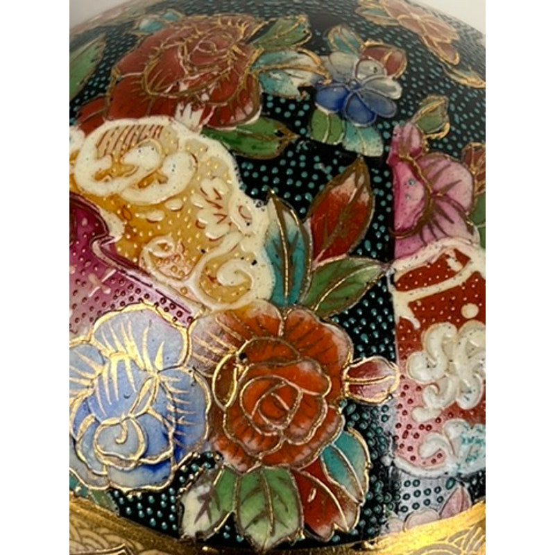 Close-up of a Large Antique Satsuma Porcelain Egg, a Chinese export collectible featuring colorful, intricate floral patterns with red, blue, and white flowers outlined in gold on a textured dark background. Brand: Unknown.