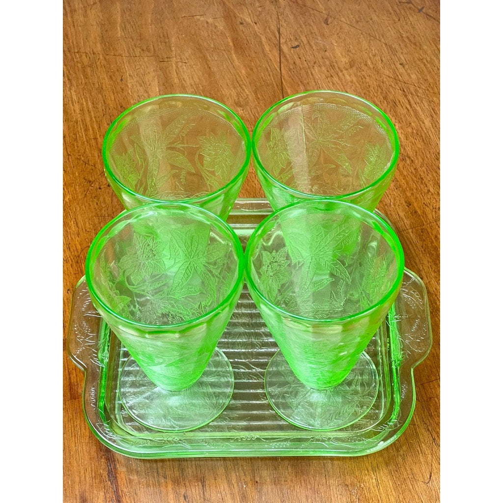 An Antique Jeannette Glass Co. Green Uranium Floral Poinsettia 5-piece beverage set from the 1930s, featuring etched cups on a matching tray, is displayed on a wooden surface.
