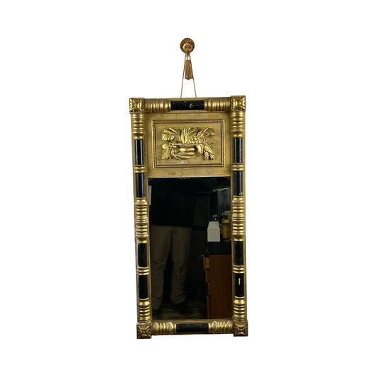 Antique Federal Period giltwood mirror c.1830 with rosette corners, gold and black neoclassical frame, cornucopia relief at top, round finial for hanging; lower glass reflects part of a person and room. Brand: Unknown.