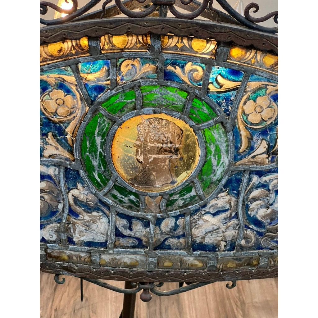 A close-up of an ornate stained glass panel in blue, green, and yellow, bordered by metalwork—evoking the Antique Five Burner Lucerne Whale Oil Lamp with Napoleon I Fireplace Screen Shade. Brand: Unknown.