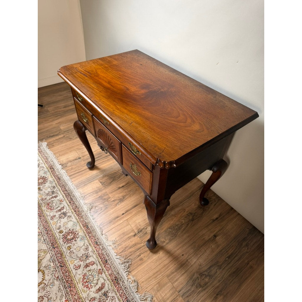 An 18th Century American Queen Anne Walnut Shell-Carved Lowboy (c. 1740–1770), this antique wooden side table with intricate carved details and two drawers stands on a wood floor near a patterned rug and an off-white wall.