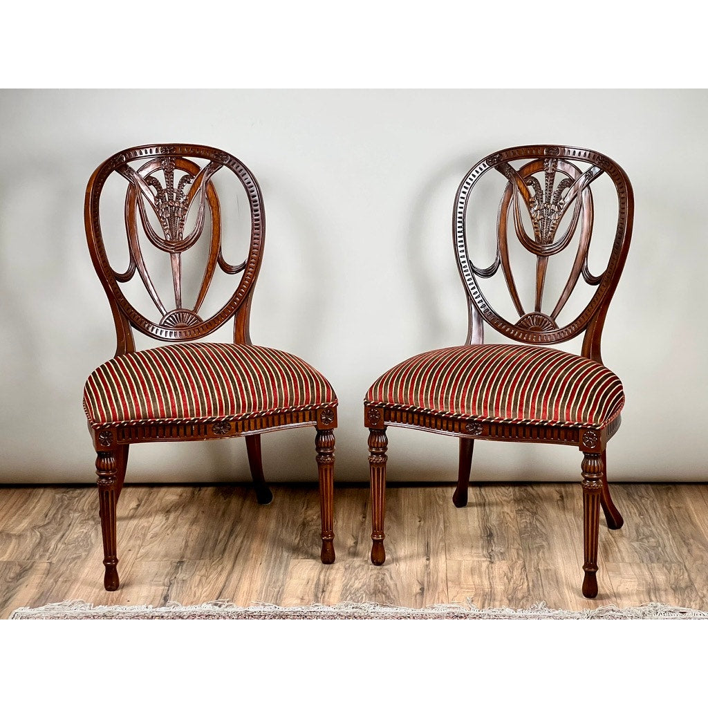 A vintage pair of Ardley Hall Wheel Back Side Chairs with carved backs and red-and-black striped seats by Ardley Hall, arranged on a wooden floor against a plain white wall, exemplify classic English design.