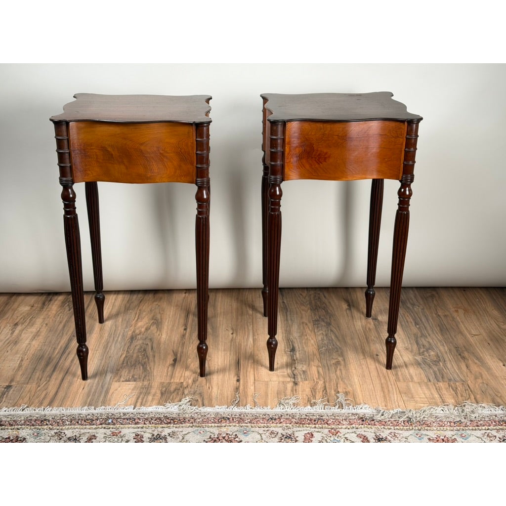A pair of American Classical Revival Mahogany Two-Drawer Work Tables, circa 1880–1910, featuring tall, dark wood, scalloped tops, two drawers each, and slender, fluted legs.