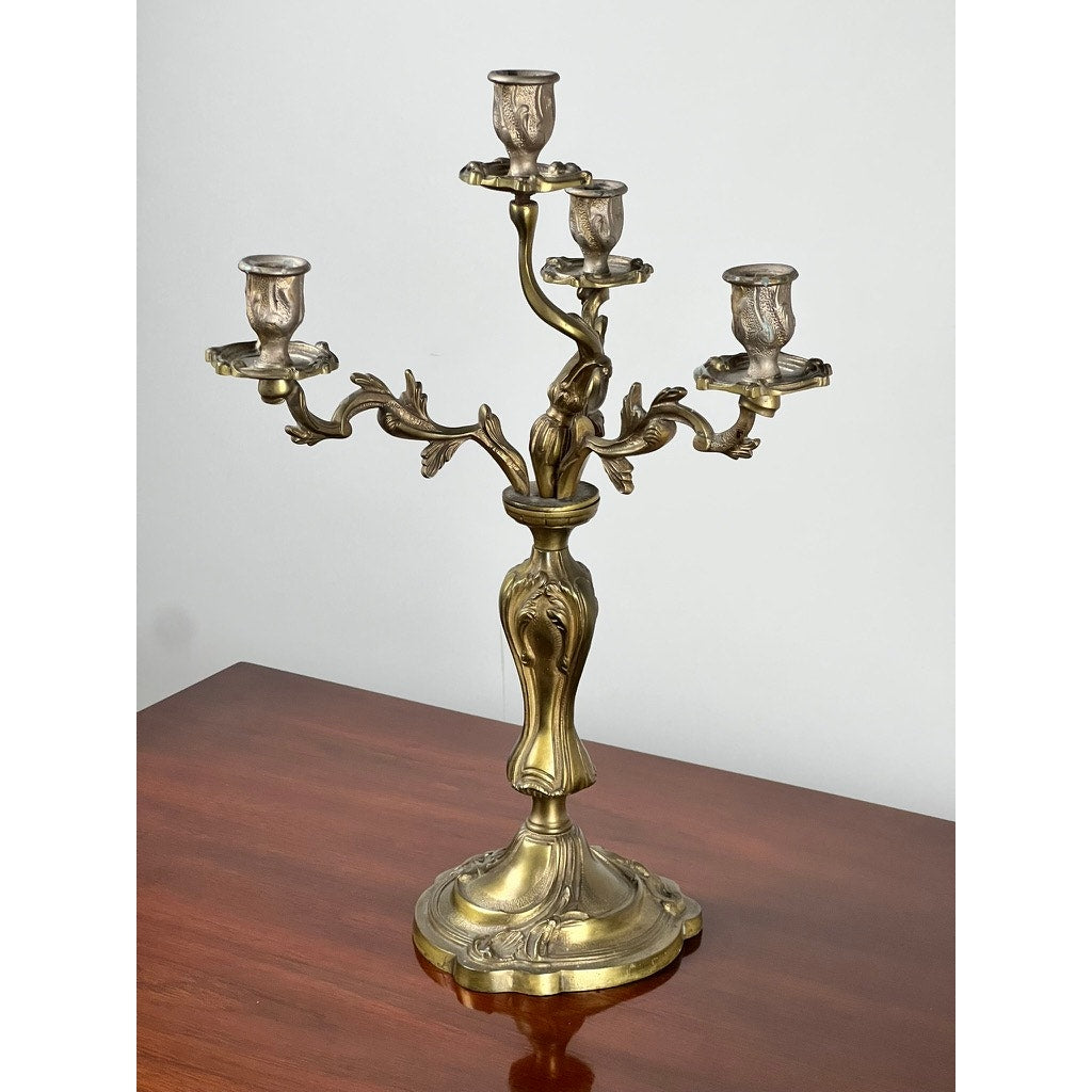 A vintage brass Louis XV style four light candelabra, brand unknown, is displayed on a polished wooden surface against a plain white background.