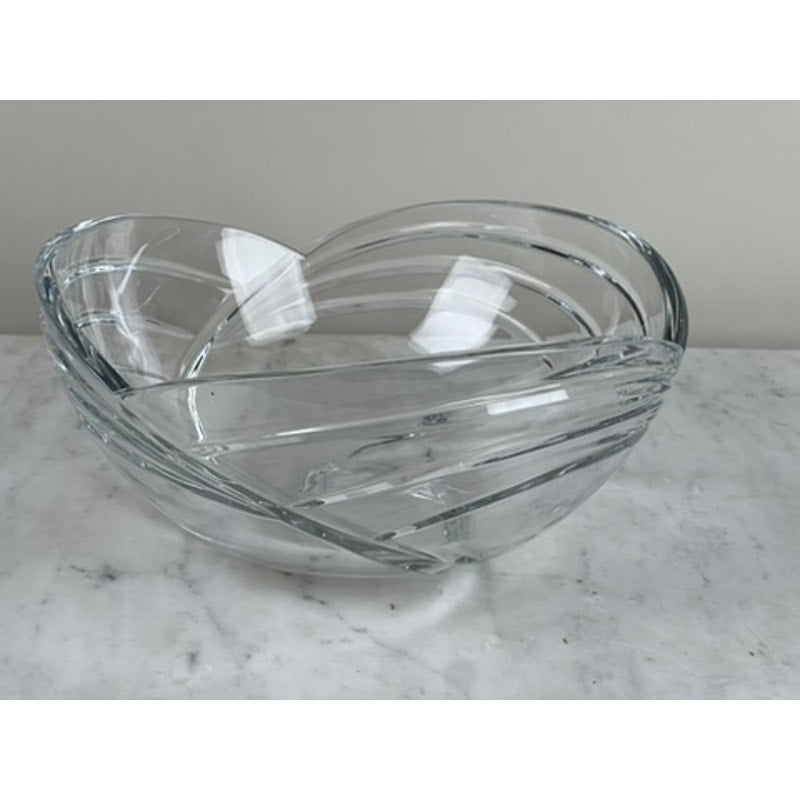 The Rogaska Samba Wave 10" Lead Crystal Bowl, featuring an abstract swirl design, sits on a white marble surface against a light wall, highlighting European luxury craftsmanship by Rogaska.