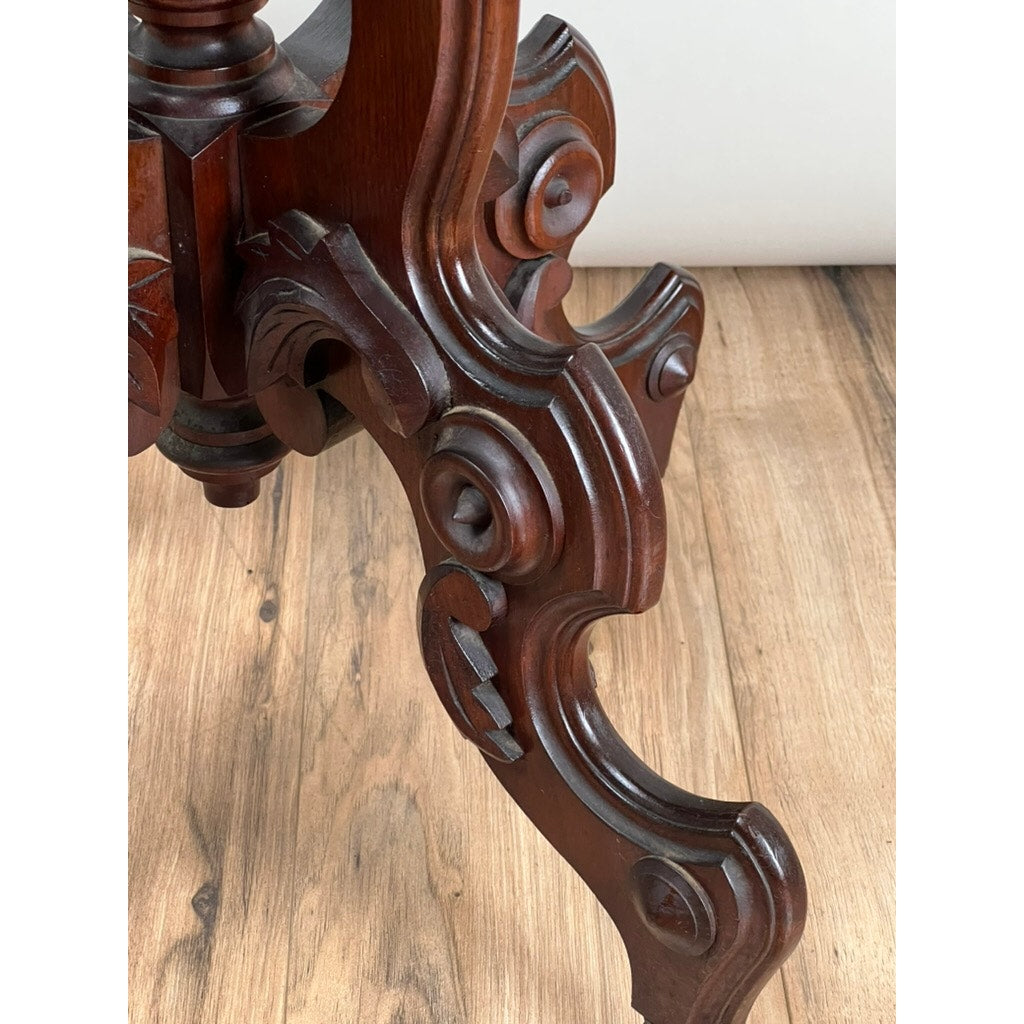 Close-up of ornate scrollwork on a late 19th-century Antique Victorian Walnut Lamp Stand with decorative carved accents, shown on a light wood floor. The polished dark wood highlights this unique accent piece. Brand: Unknown.