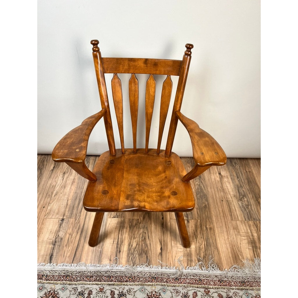 A Cushman Vintage Herman DeVries for Cushman No. 5-82 Rock Maple Easy Chair with a spindle back and contoured seat sits on a wood floor near the edge of a patterned rug.