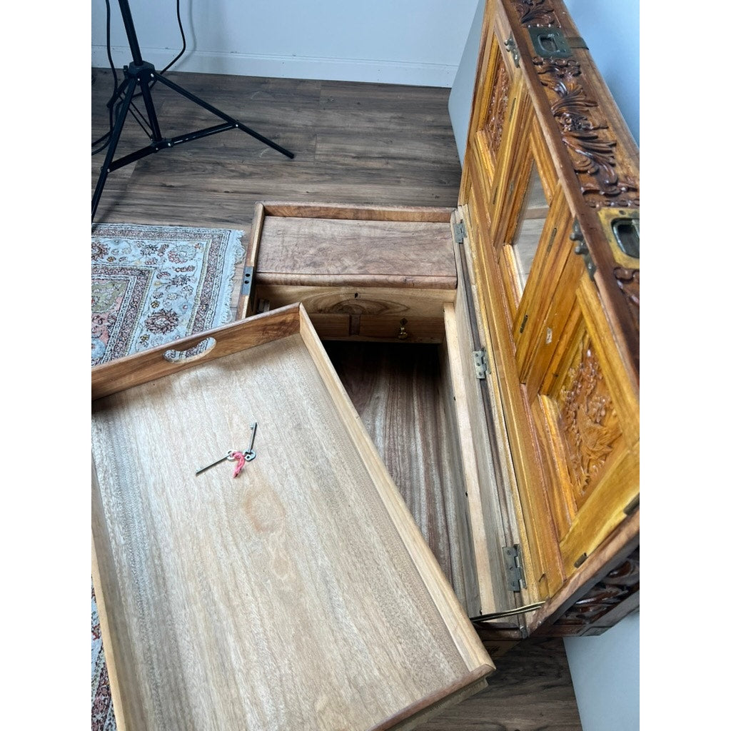 A Chinese Export Carved Camphor Wood Dowry Chest with open drawers and doors reveals a set of keys resting on an open drawer. Reminiscent of a hand-carved dowry chest, this piece sits atop a wooden floor, with part of a patterned rug and a tripod stand visible nearby. Brand: None/Unknown.