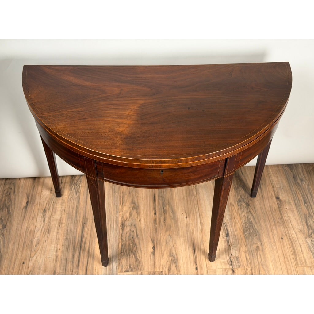 An English George III Mahogany and Satinwood-Inlaid Demilune Games Table, circa 1790–1810, featuring light wood inlay on the semi-circular mahogany top and apron, supported by four tapered Hepplewhite style legs.