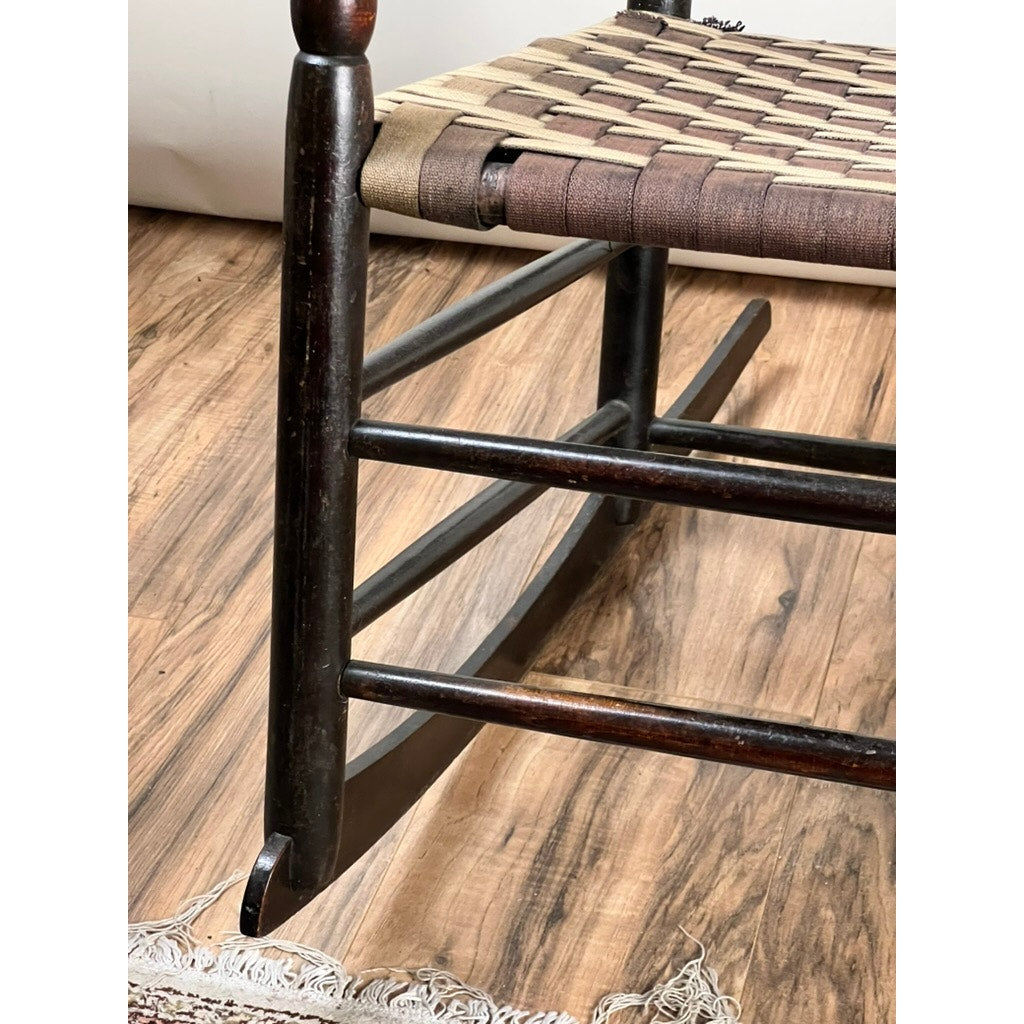 Close-up of the lower part of an Antique Shaker #6 Tape Seat Rocker by Mt. Lebanon Shakers, c. late 19th century—showing its curved runners, woven seat, and a rug on a wooden floor; a fine example of Shaker craftsmanship.