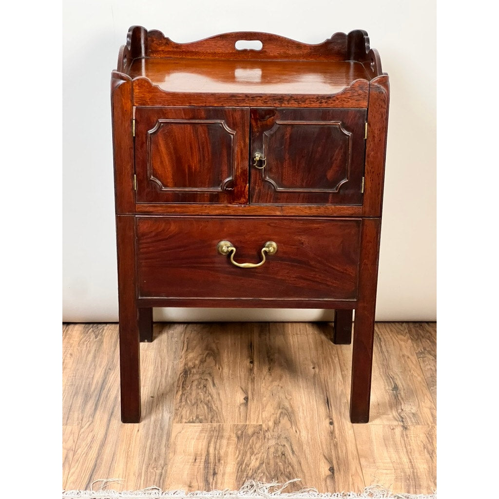 This Antique George III Bedside Commode, dating to the late 18th century, features paneled cabinet doors, a single drawer with brass handle below, a pull-out leather surface, and stands on four straight legs. Brand: Unknown.