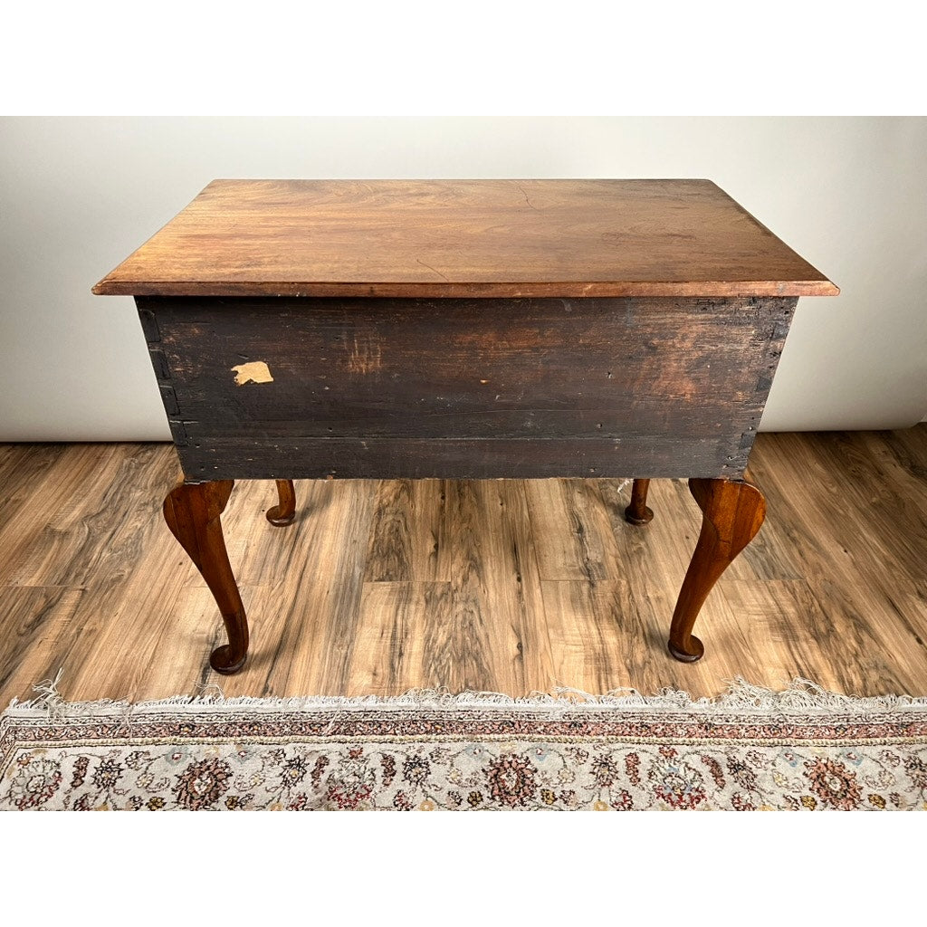 An Antique George III Queen Anne Mahogany Lowboy from the late 18th century, featuring a lighter wood top, dark weathered sides, and four curved legs, stands on a wood floor with part of a patterned rug in front.