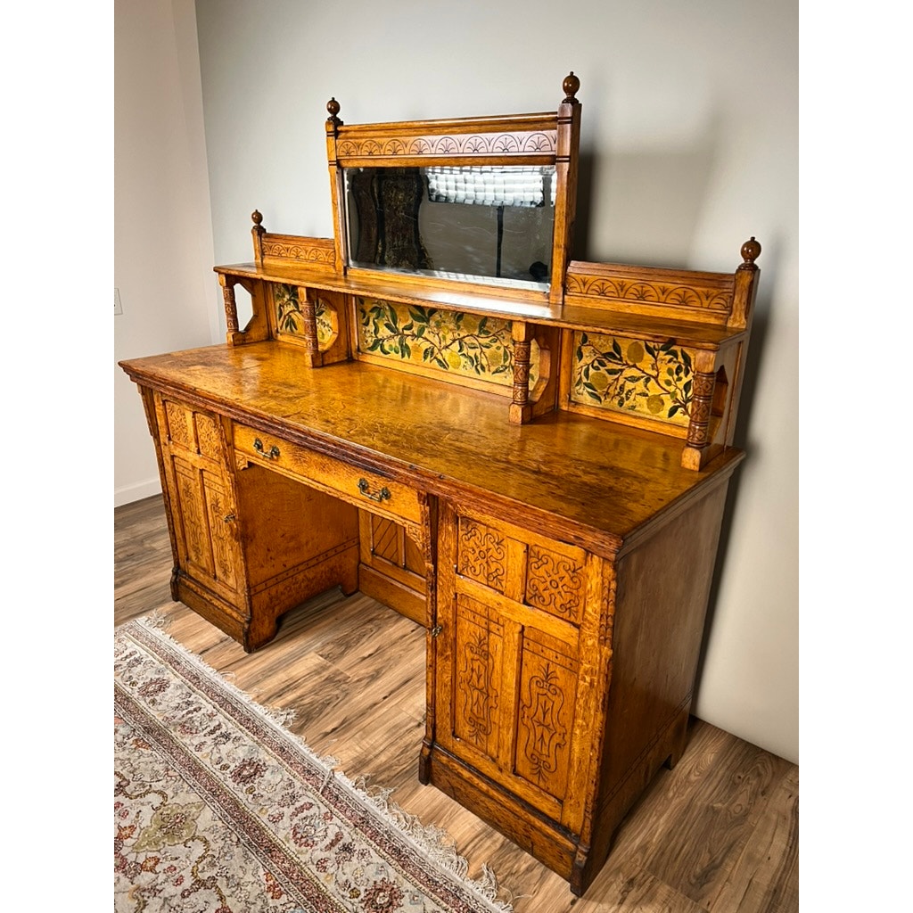 An Antique Victorian Aesthetic Movement Oak Desk in original finish (late 19th century) stands on a wood floor near a patterned rug against a plain light wall, showcasing period elegance with decorative carvings and historic charm.
