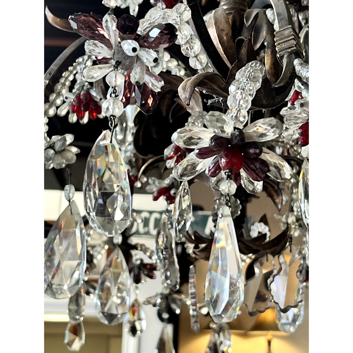 Close-up of an antique late 19th-century French Rococo tole amethyst and crystal ten-light chandelier, adorned with amethyst and clear crystals, metal leaves, and hanging prisms against a soft, blurred background.