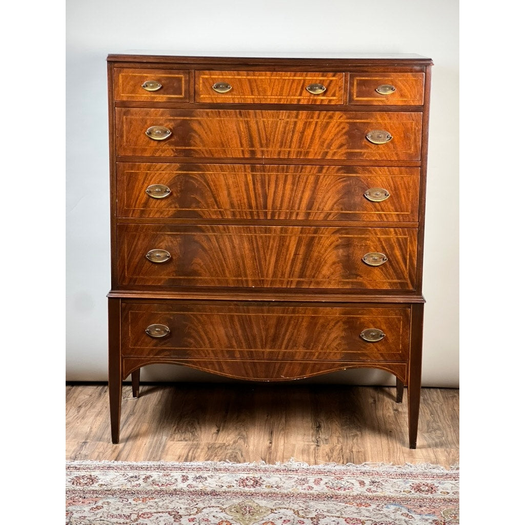 Vintage Dutch Woodcraft Shops Federal Style Flame Mahogany Chest on Stand, circa 1945–1955, featuring six drawers with brass handles, a striking flame mahogany wood grain pattern characteristic of Federal styling, and elegantly tapered legs. The chest sits atop a wood floor partially covered by a patterned rug, exemplifying the renowned craftsmanship of Dutch Woodcraft Shops.