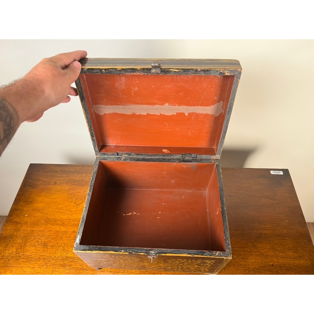 A hand lifts the lid of an empty Antique New England Folk Art Painted Portrait Document Box, Mother & Child, c. 1840–1860, its worn exterior and red interior displayed on a wooden surface. Brand: None/Unknown.