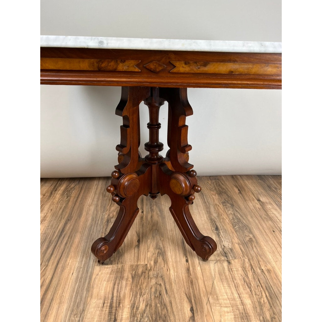 Antique Eastlake Victorian Walnut Marble Top Stand, late 19th century, features a carved central base and marble top, displayed on a light wood floor against a plain pale wall. Brand: None/Unknown.