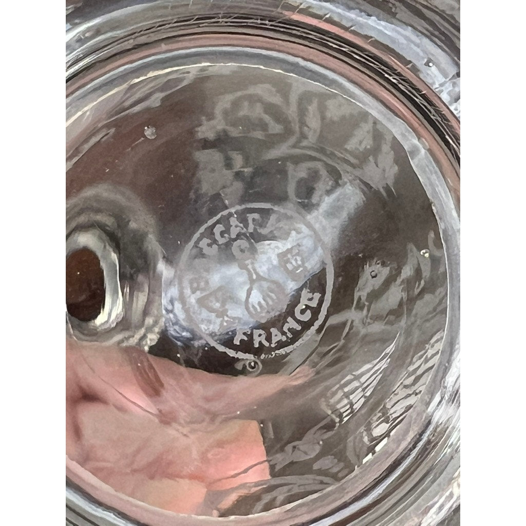 Close-up of a vintage Baccarat crystal decanter base in the "Michelangelo" pattern for Martell Cognac c. 1930 shows the etched “Baccarat France” logo with a decanter and glass symbol, along with visible reflections and a hand.