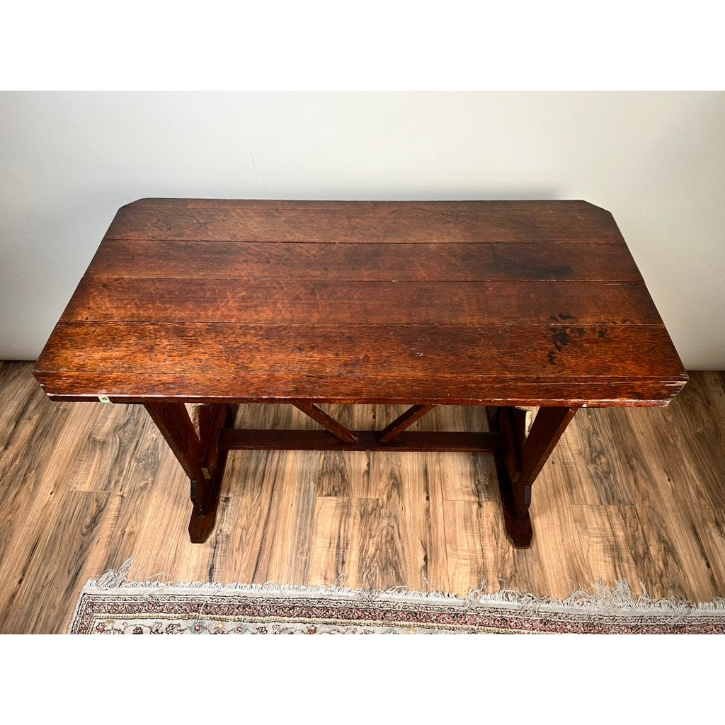 An Antique Rustic Italian Fratino Trestle Table from the late 19th century with a rich dark finish and sturdy crossed support beams stands on a wood-patterned floor beside a patterned rug. Brand: unknown.