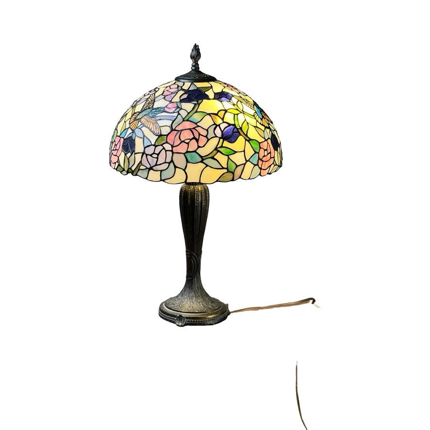 The Vintage Tiffany Style Floral Stained Glass Table Lamp features a dome-shaped shade with floral and butterfly patterns, an ornate bronze-toned base, and a plug-in cord. Brand is unknown.