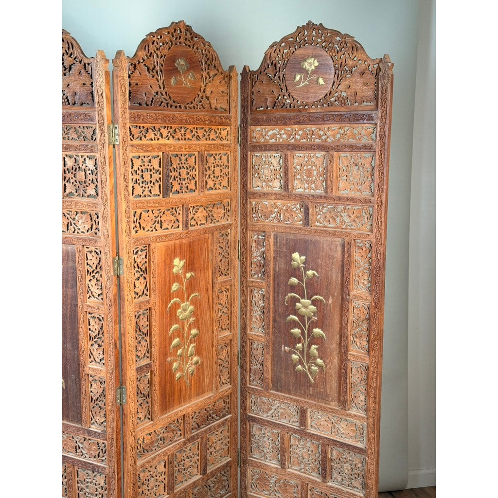 This Early 20th Century Anglo-Indian Carved Teak Four-Panel Screen from Pearl City Antiques boasts ornate, arched tops and exquisite applied brass floral decoration. Each panel features intricate carvings with two sections adorned in greenish floral designs, capturing the refined elegance of a traditional decorative folding screen.