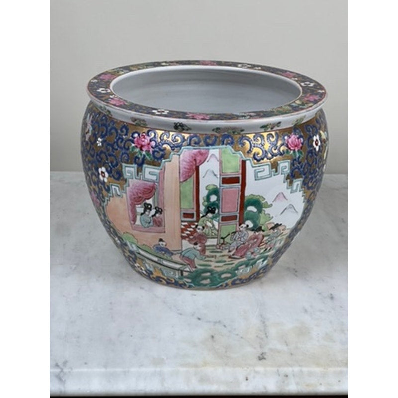 A hand-painted Vintage Chinese Famille Rose Fish Bowl signed Minicucci, featuring colorful traditional figures, florals, and geometric patterns, sits as a statement planter on marble against a plain background.