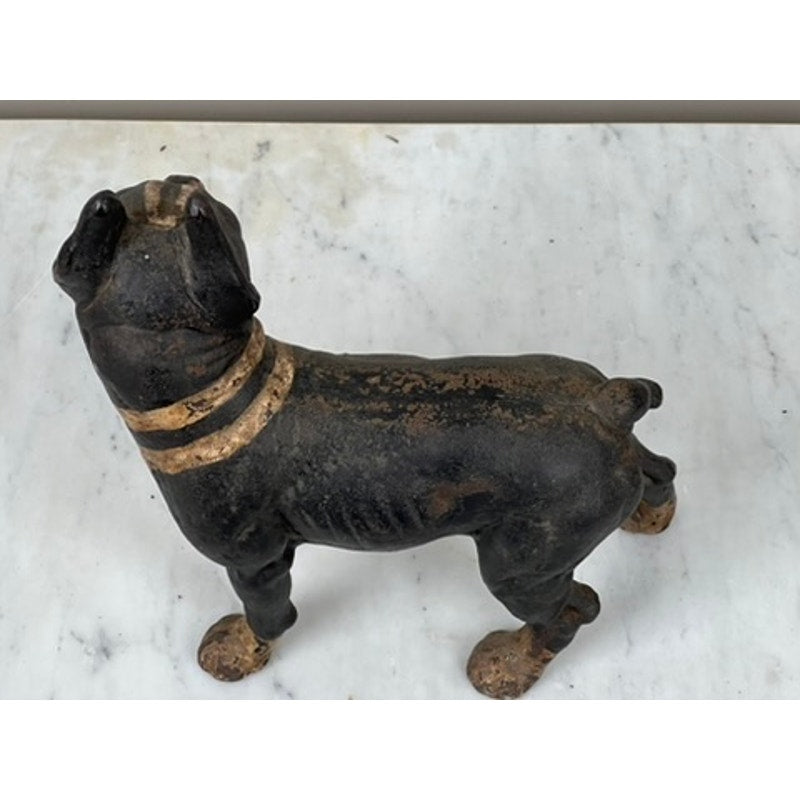 A vintage Hubley Antique Cast Iron Boston Terrier Doorstop with tan accents stands on a light marble surface, facing away and slightly to the side.