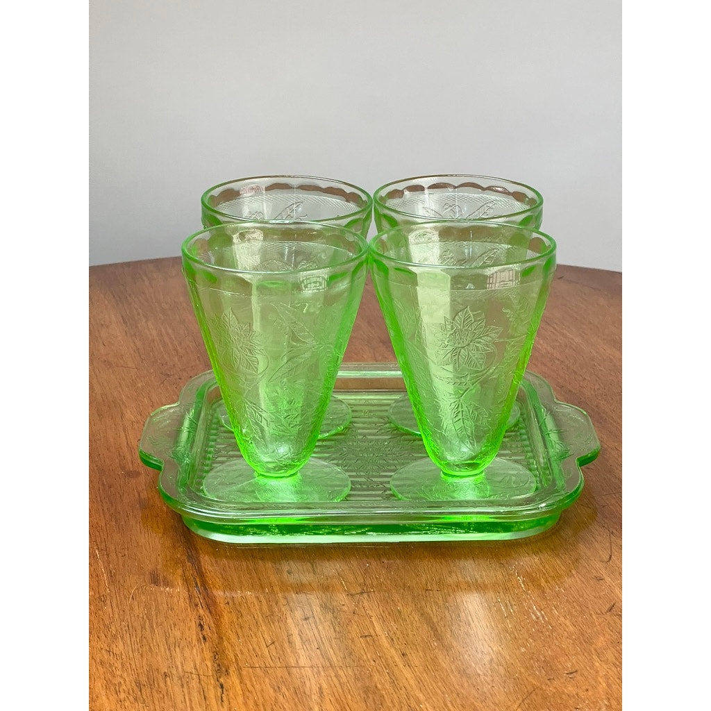 The Antique Jeannette Glass Co. Green Uranium Floral Poinsettia 5-Piece Beverage Set (c. 1930s) features four etched tumblers and a matching tray, elegantly displayed on a wooden surface with a neutral background.