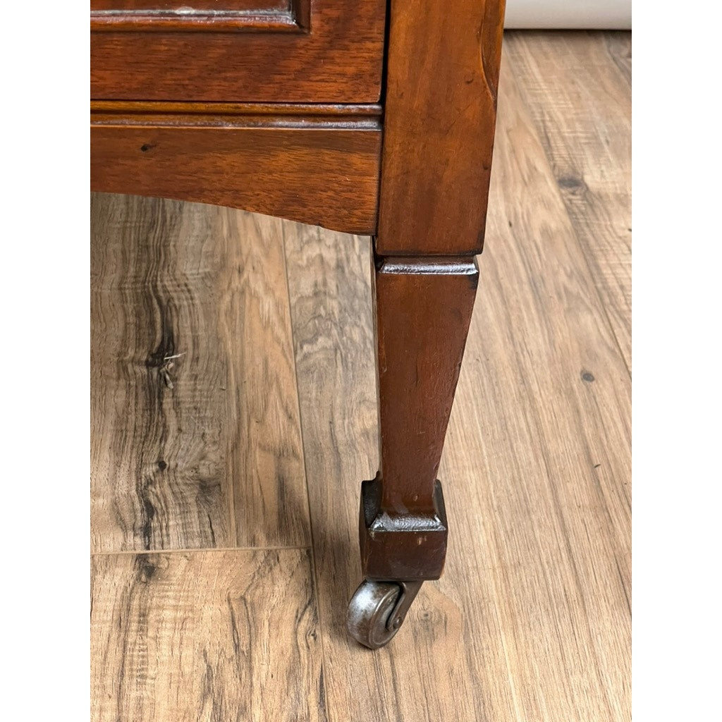 Close-up of a leg from an Antique Depression Era Mahogany Two Over Three Chest of Drawers c. 1930s, featuring a metal caster, polished reddish-brown finish, and beveled details typical of American furniture from this period.